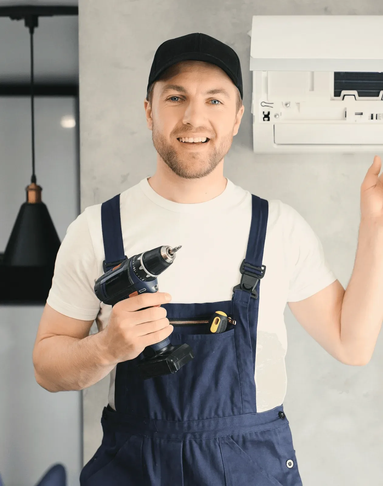 A smiling technician holding a drill beside a wall unit.
