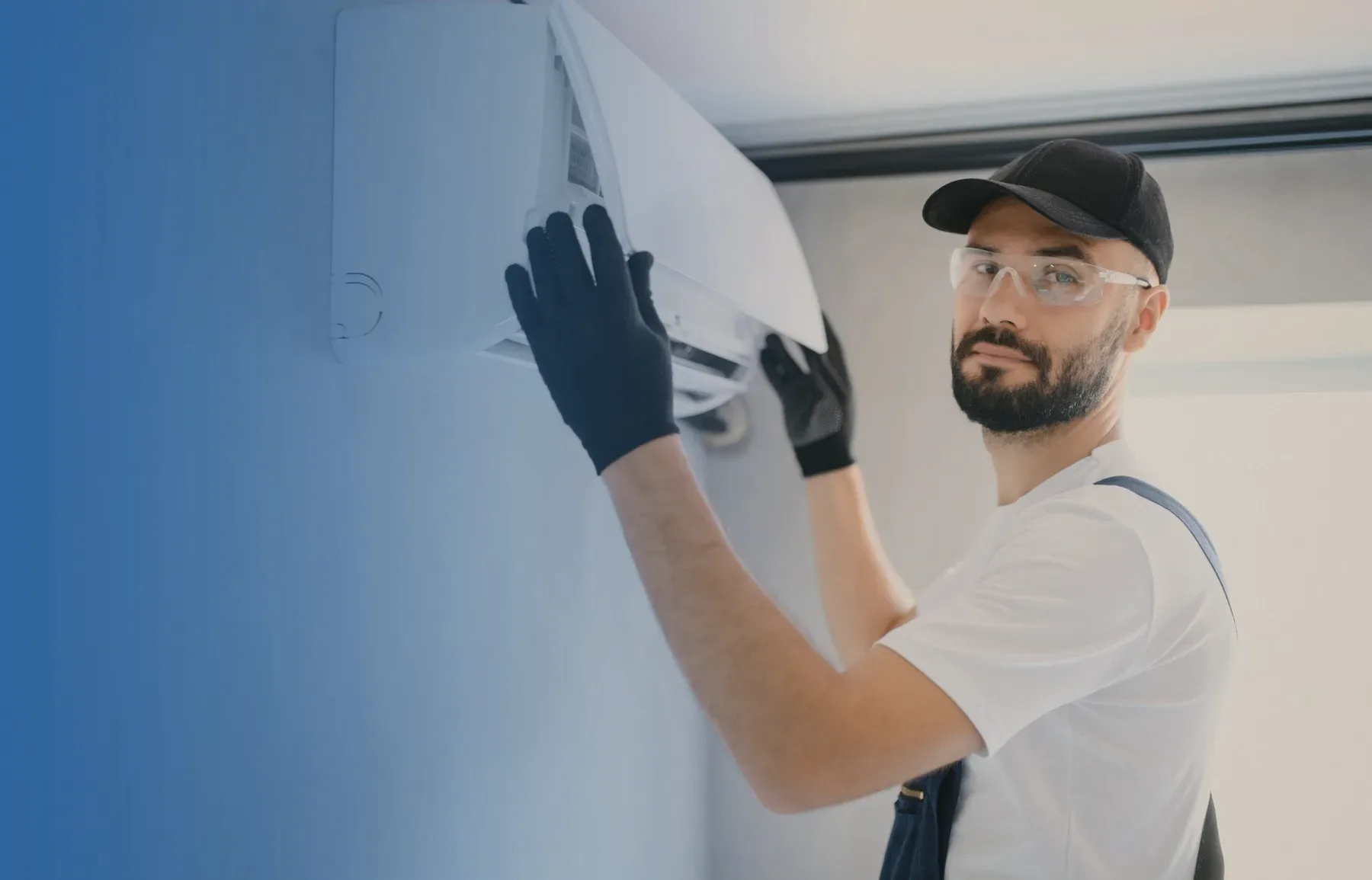 A technician in a cap and safety glasses fitting a wall unit.