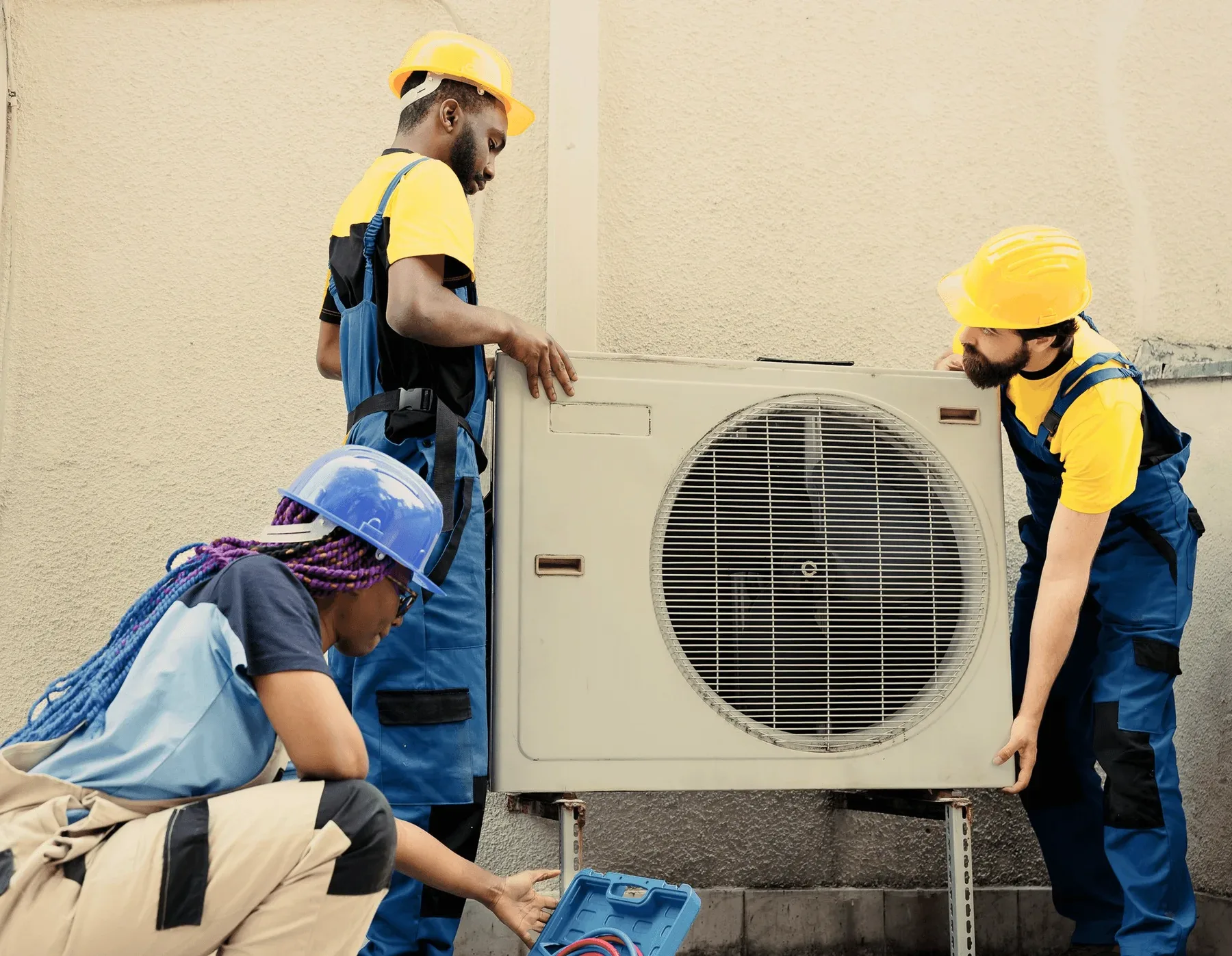 Two technicians carrying an outdoor unit past a wall.