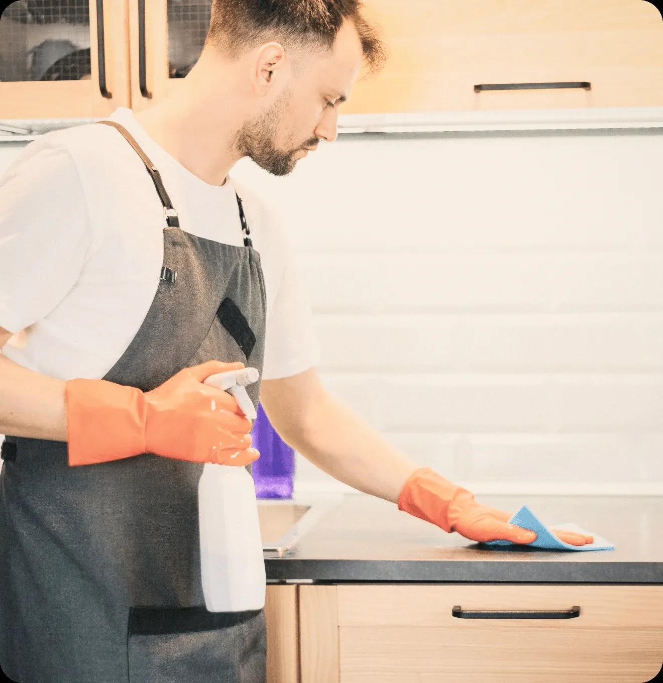 A cleaner in an apron wiping a kitchen counter.