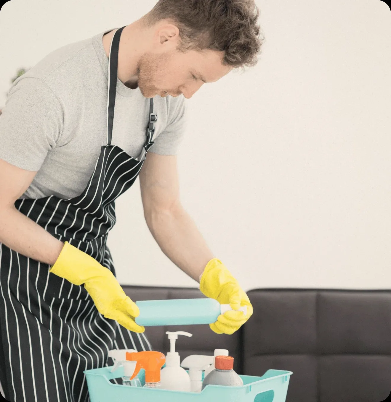 A cleaner in a striped apron with a caddy of bottles.