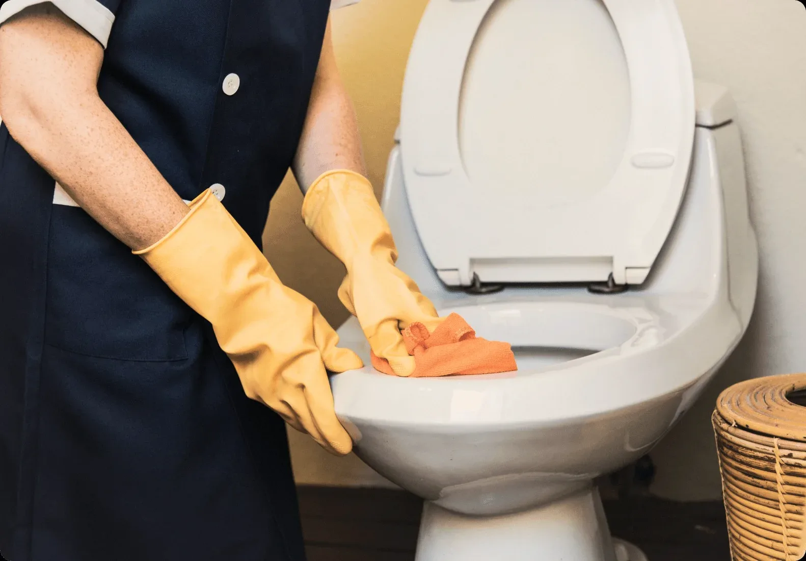 Yellow gloves wiping a white toilet.