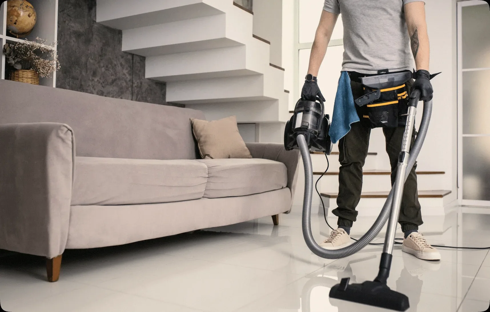 A cleaner vacuuming beside a beige sofa.