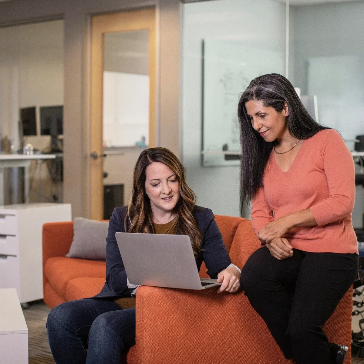 Two colleagues on an orange sofa with a laptop.