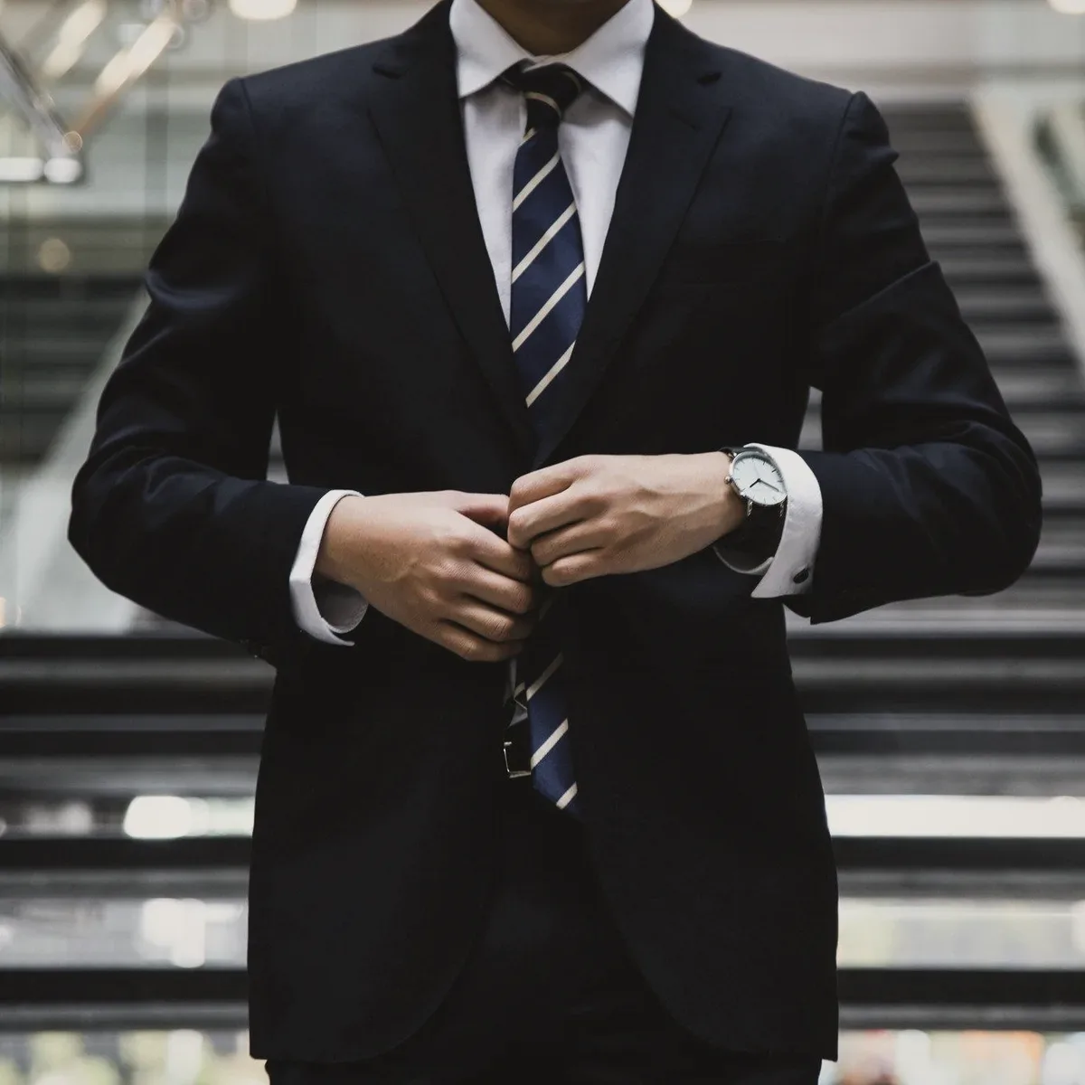 A man in a dark suit buttoning his jacket on a staircase.