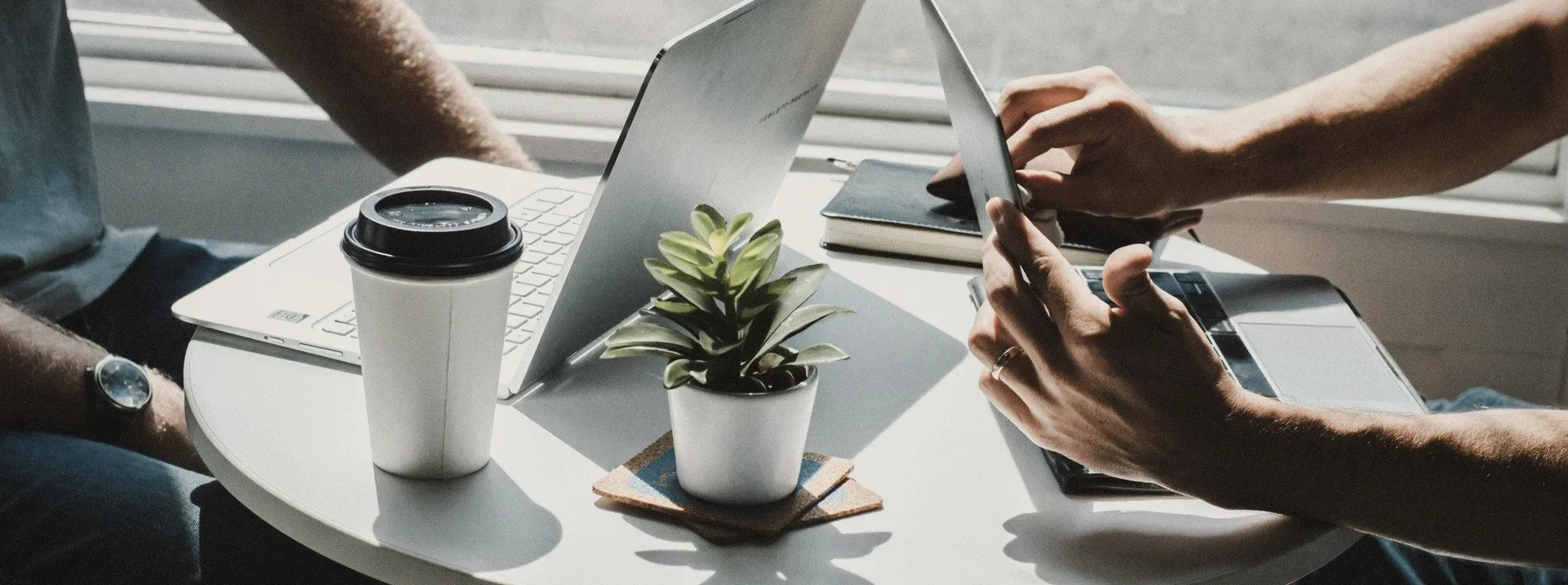 Hands over laptops and a coffee at a shared table.