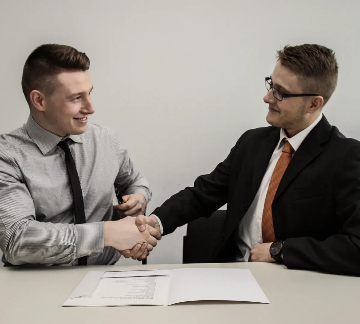 Two men shaking hands over a desk.