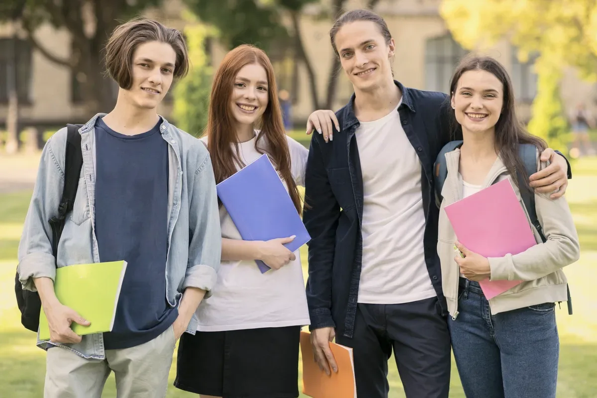 Five students with folders on a lawn.