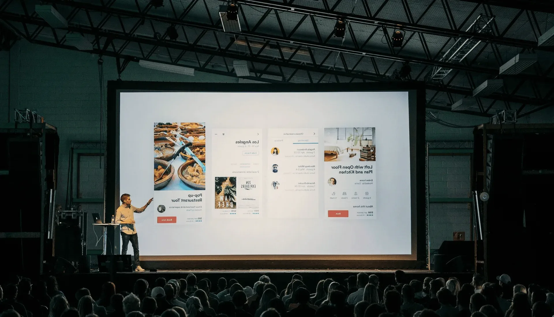 A speaker on a stage before a large screen.