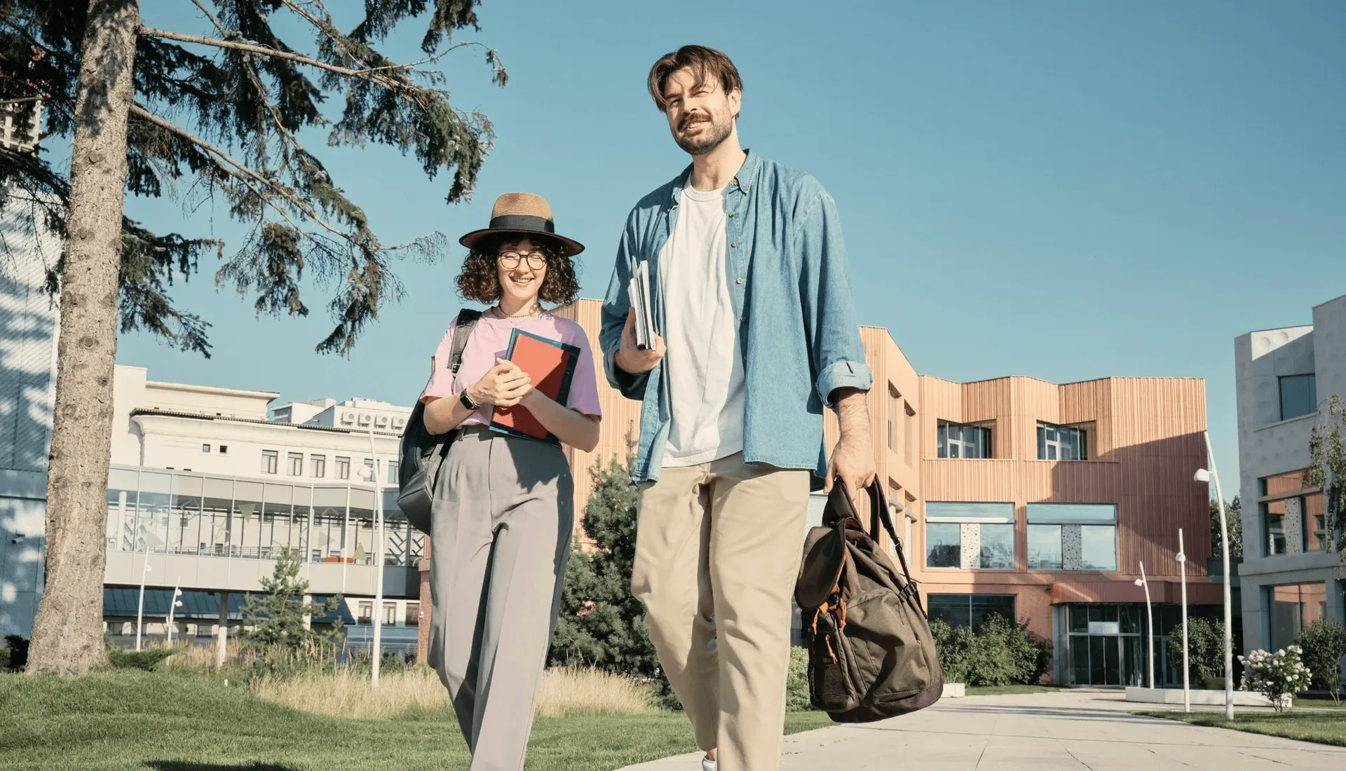 Two students with books and a bag on a campus path.