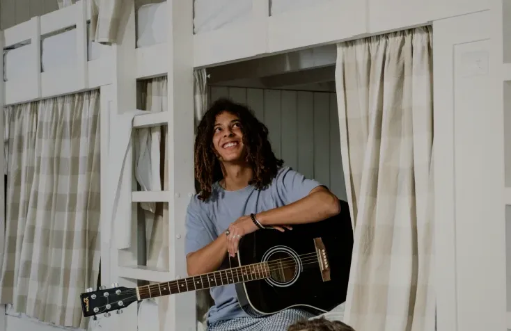 A guest playing guitar in a curtained bunk bed.