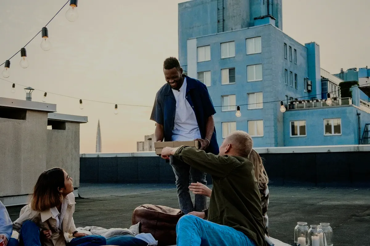 Friends sharing a pizza on a rooftop at sunset, string lights overhead.