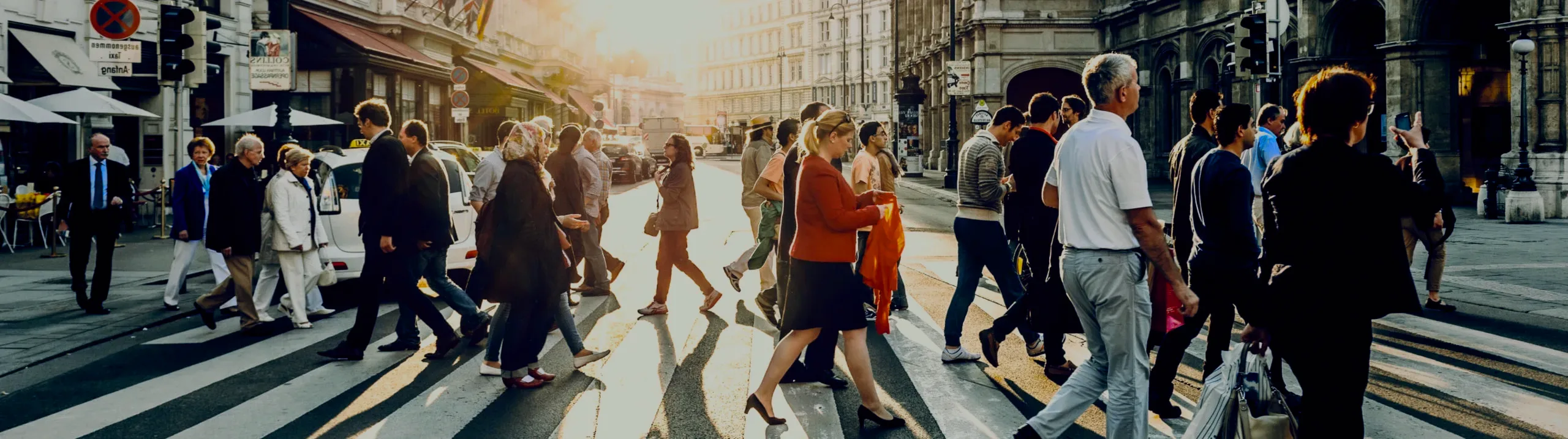 A crowd crossing a city street in the evening sun.