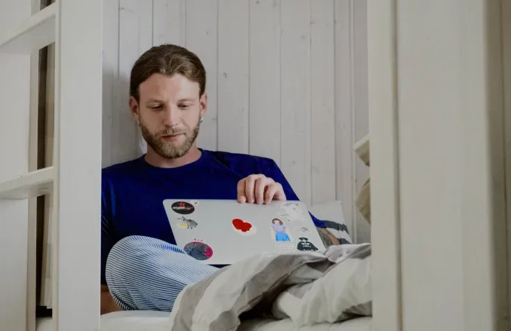 A man working on a laptop in a bunk bed.