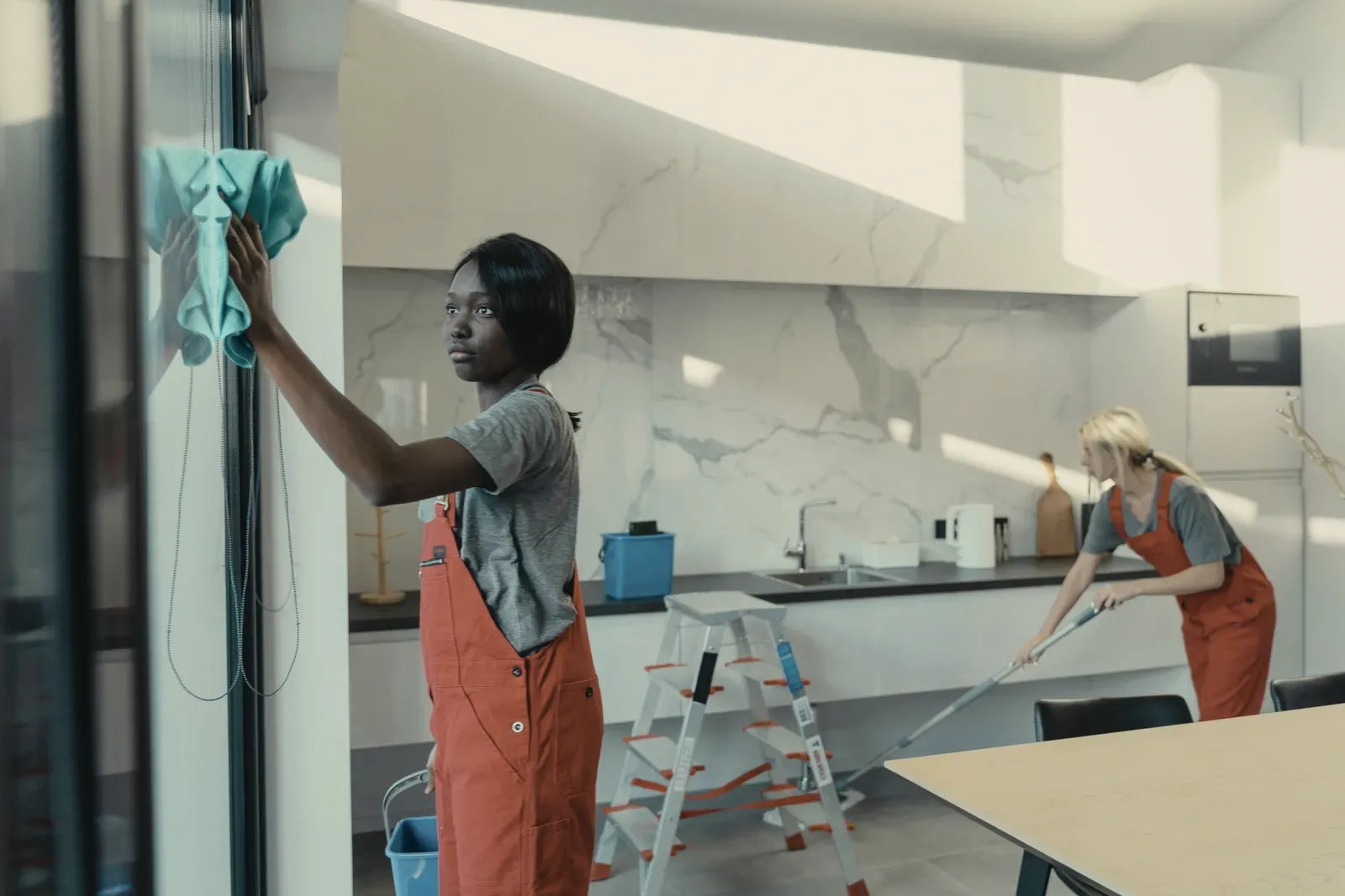 Two cleaners in red overalls at work in a white kitchen.