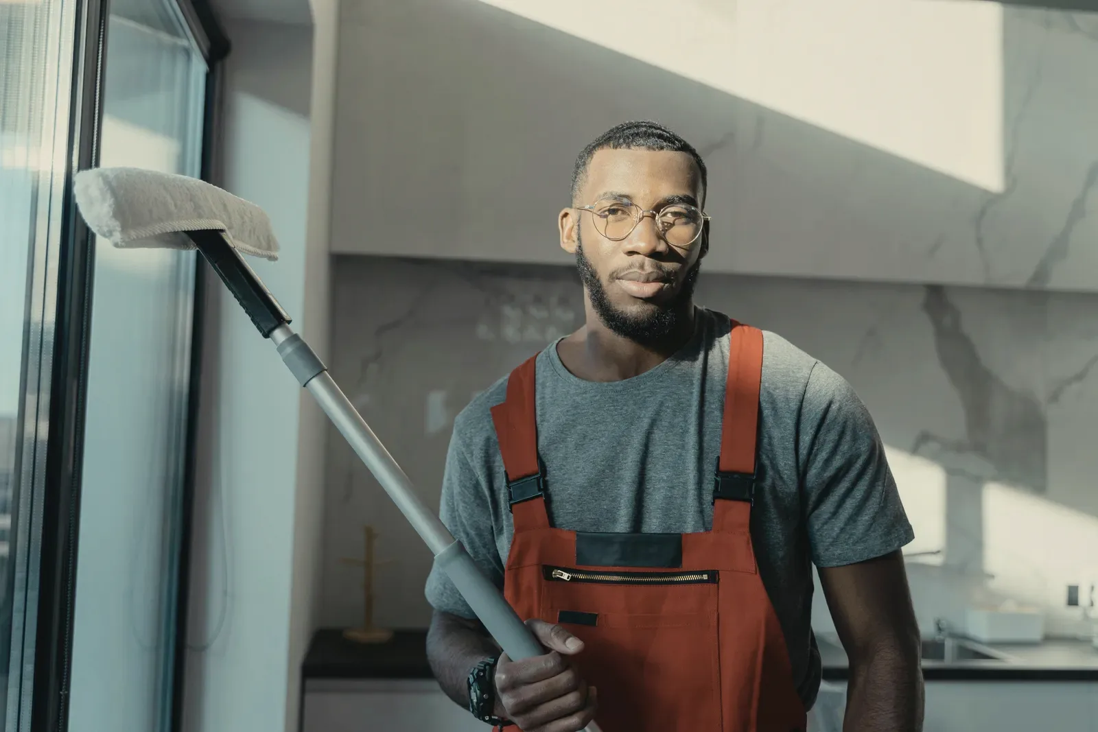 A cleaner in red overalls with a vacuum in a bright living room.