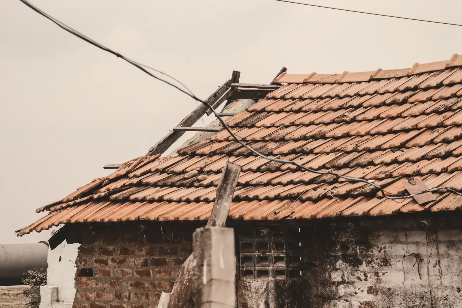 An aged tile roof with a section stripped back and tiles missing above a damaged wall.
