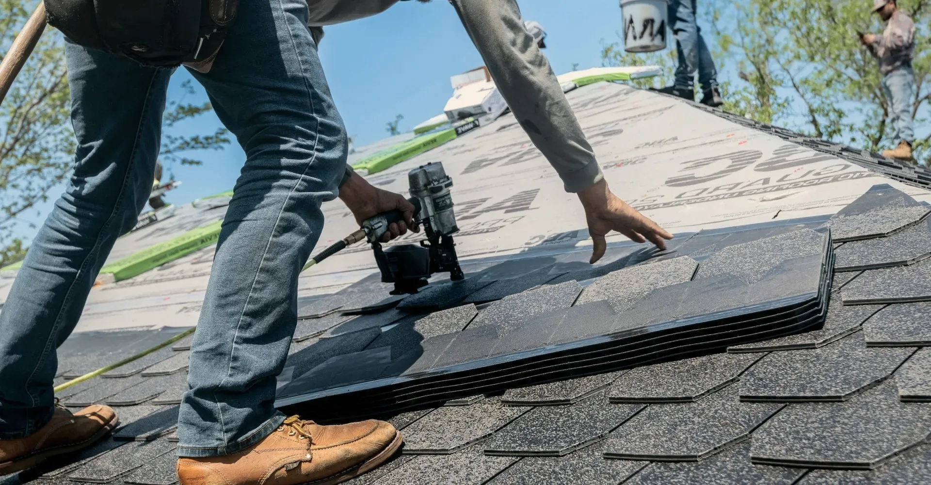 A roofer's boots and a nail gun on new shingles.