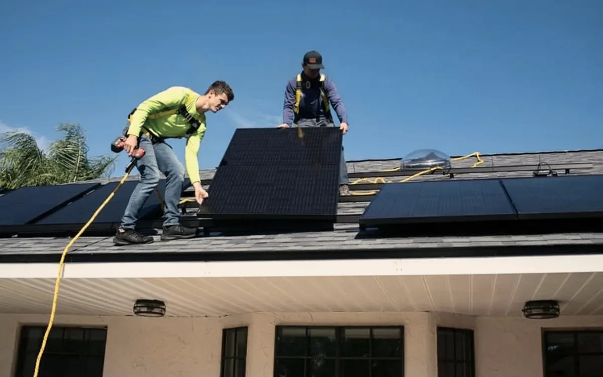 Two roofers fitting panels on a roof.