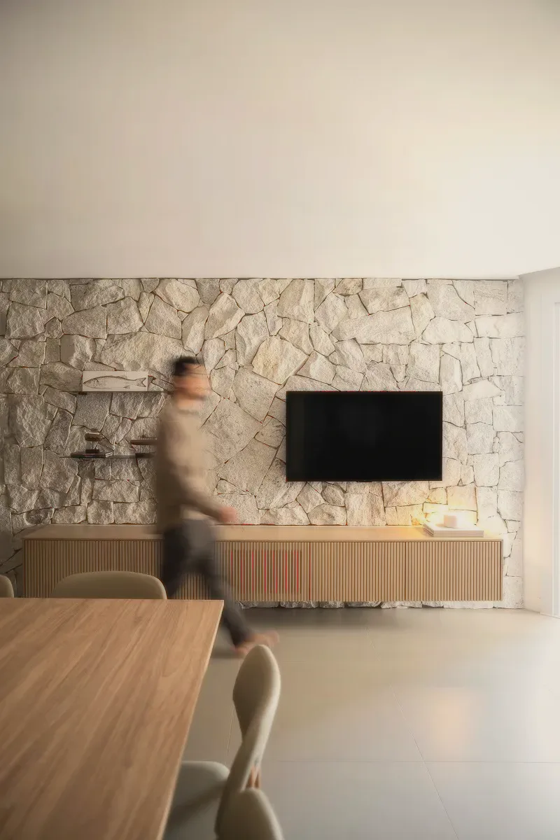A living room with a stone wall, a wall-mounted screen and a wooden cabinet.