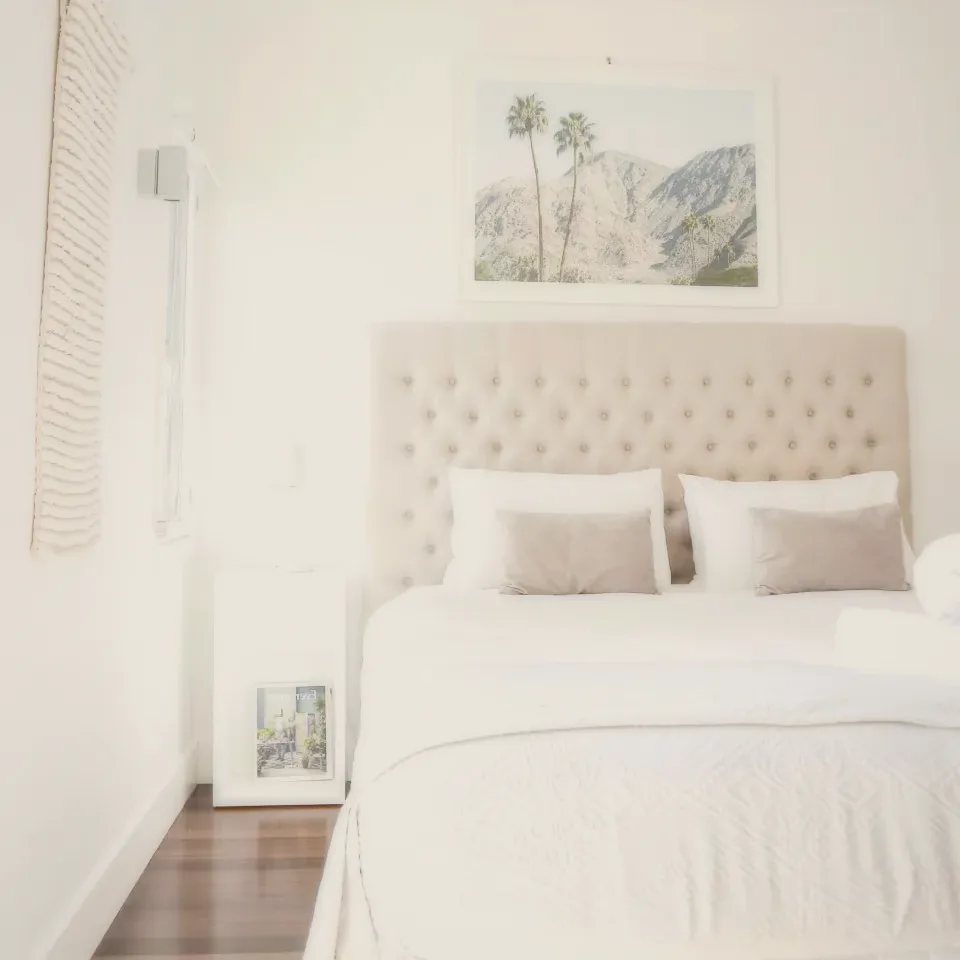 A bedroom with a tufted headboard, white bedding and a framed print.