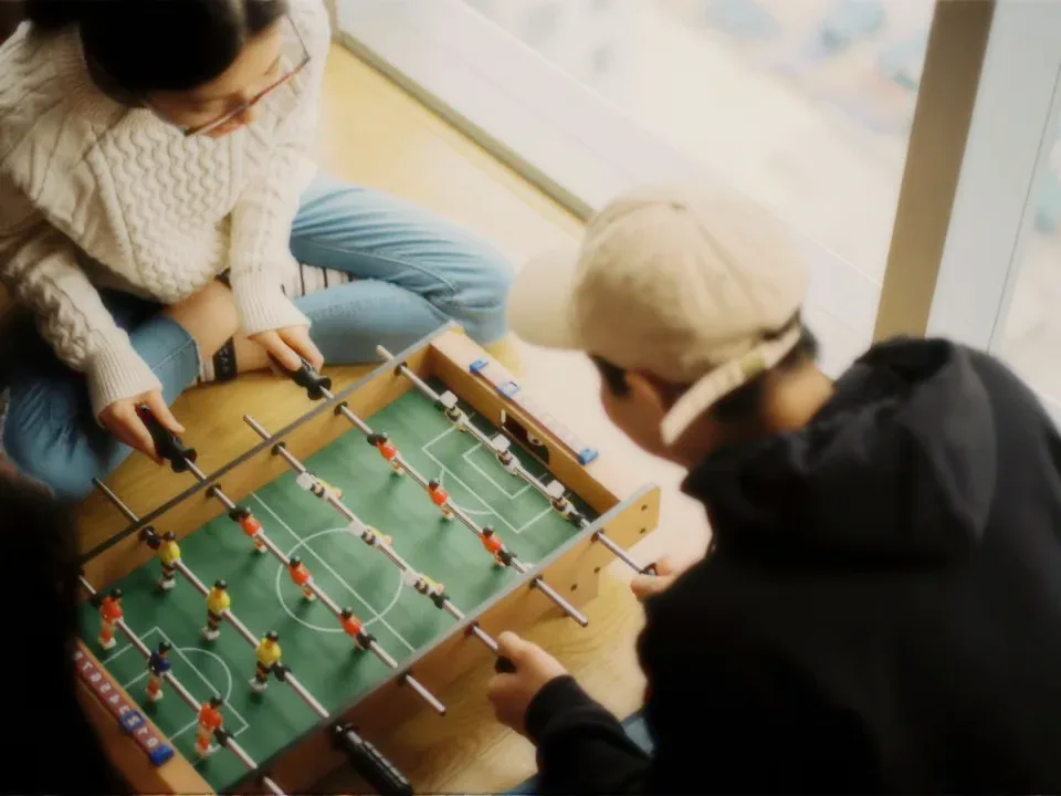 Two friends playing foosball by a window.