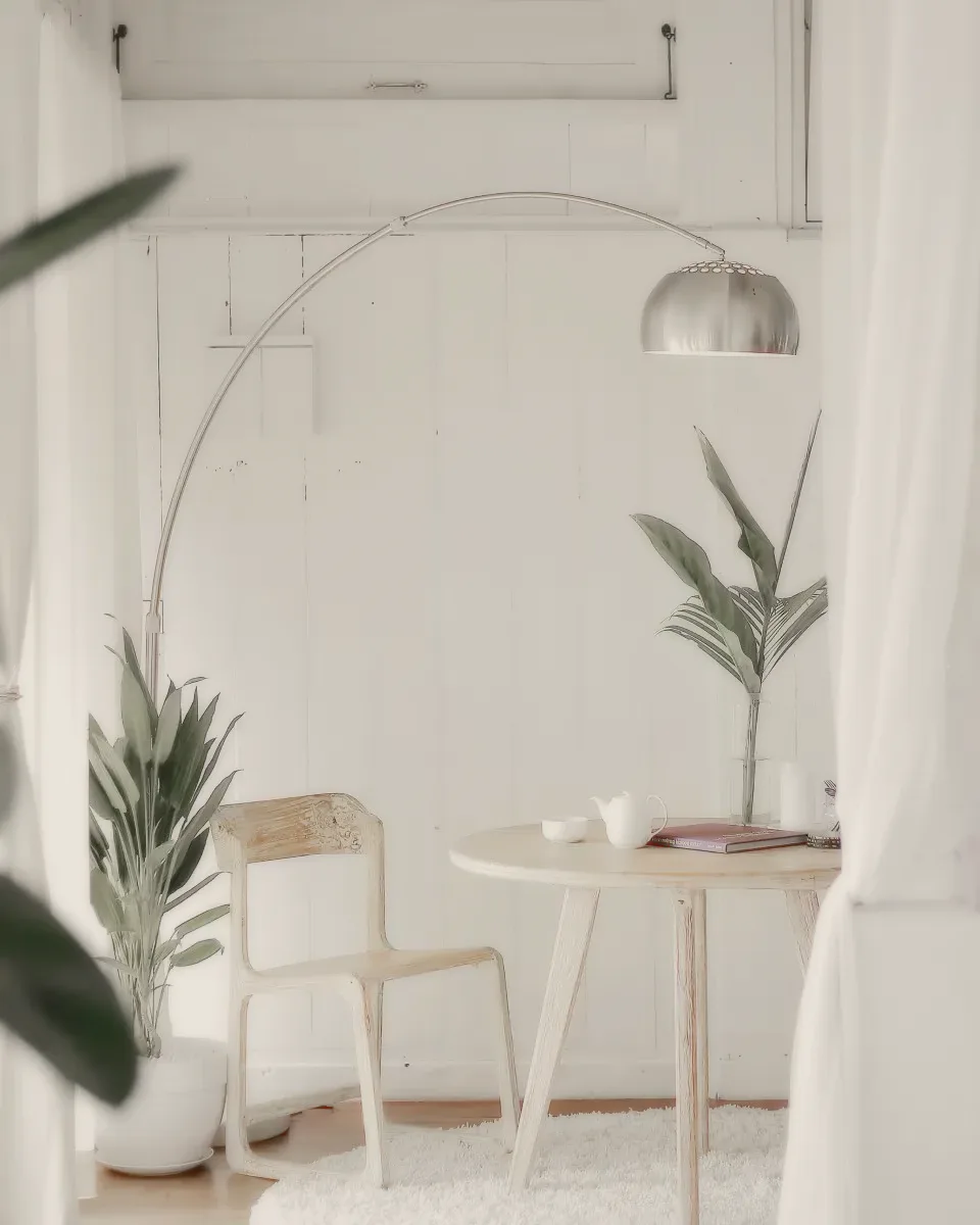 A round wooden table and one chair under an arched floor lamp.
