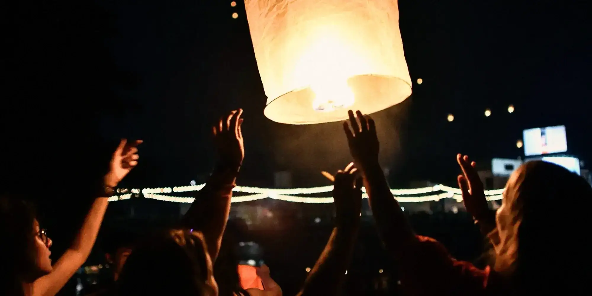 Hands reaching up to a paper lantern at night during the lantern festival.