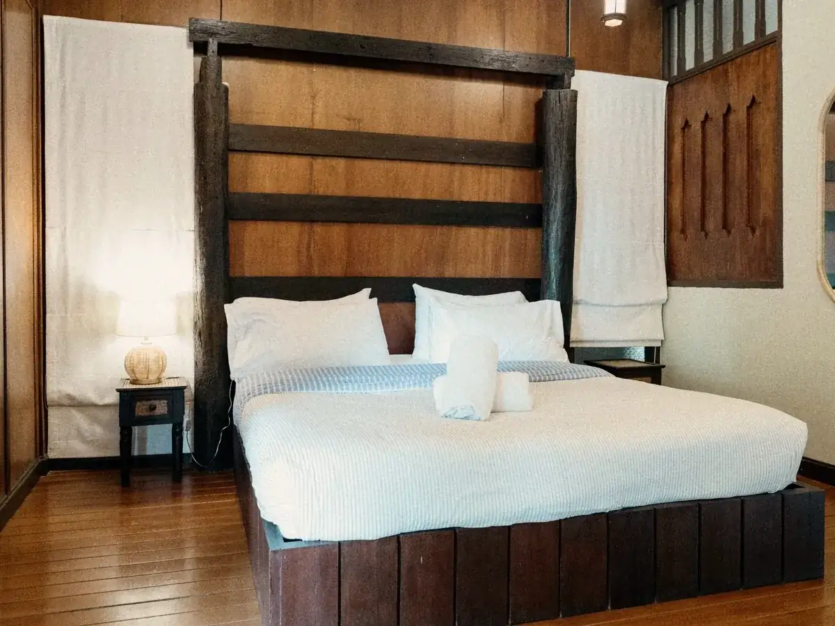 A double bed with a teak headboard and a lamp in a private room.
