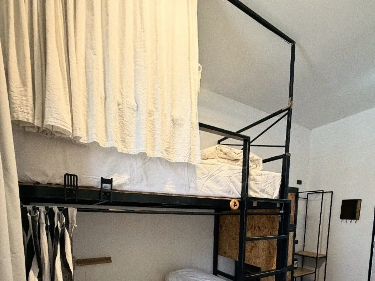 Black steel bunks with white bedding and curtains in a quiet dorm.