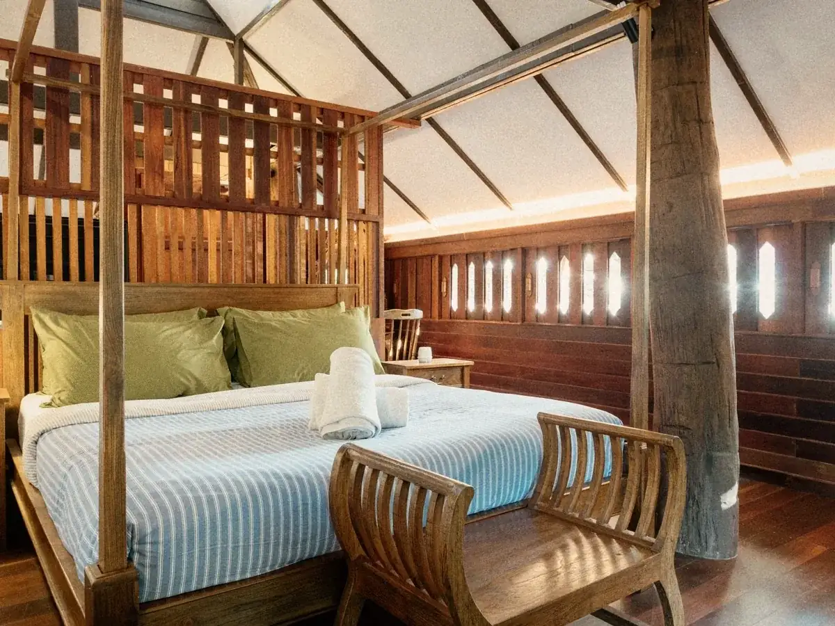 A double bed under a teak roof in a Lanna-style private room.