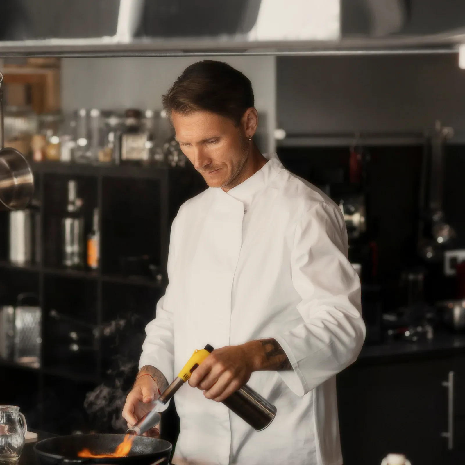 A chef in whites finishing a dish with a torch.