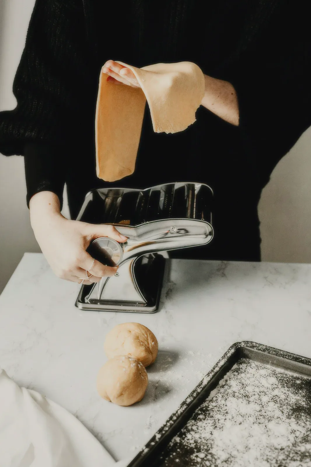 Hands turning a pasta machine on a marble counter.