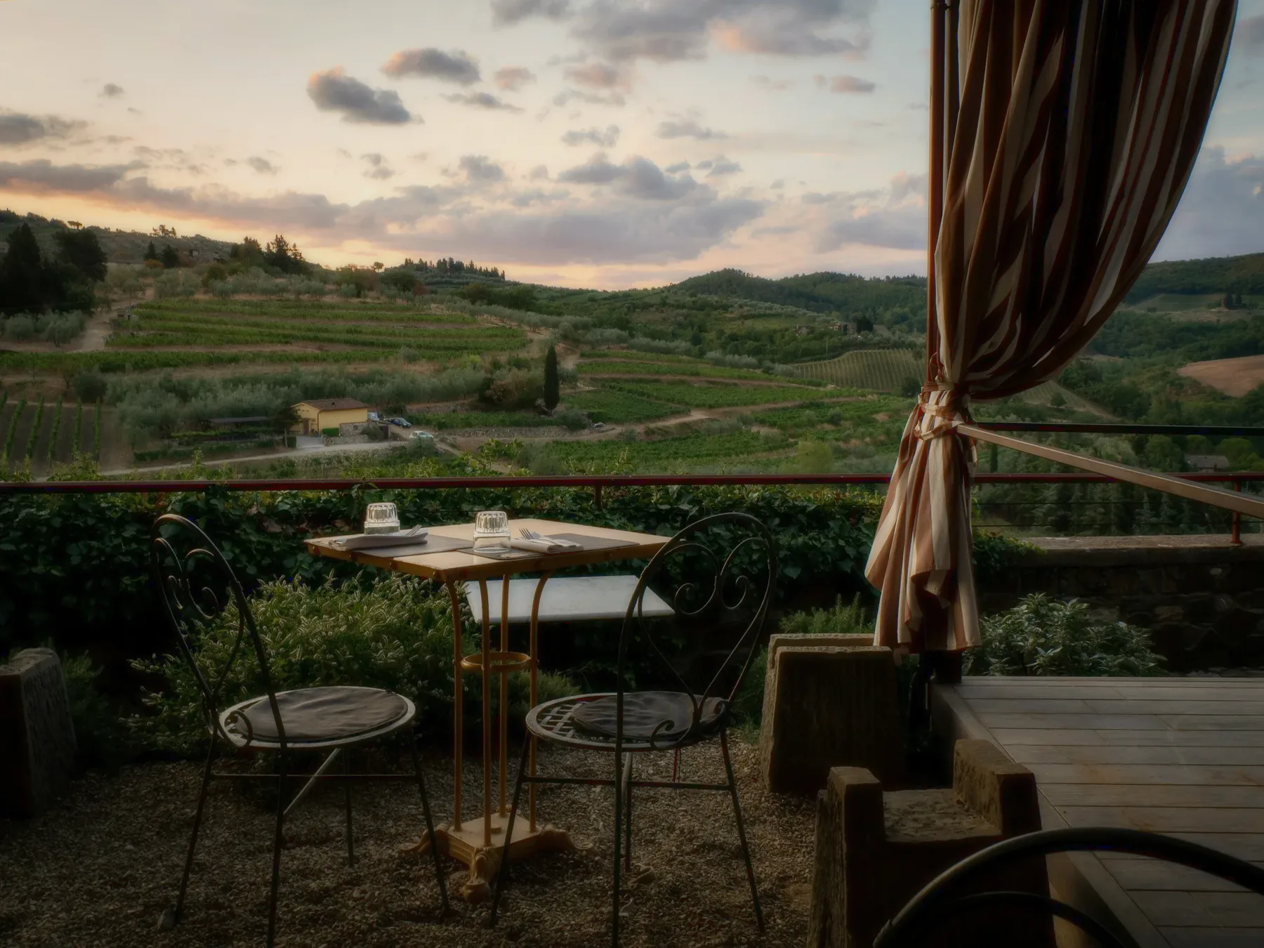 A terrace table under a striped curtain, vineyards below.
