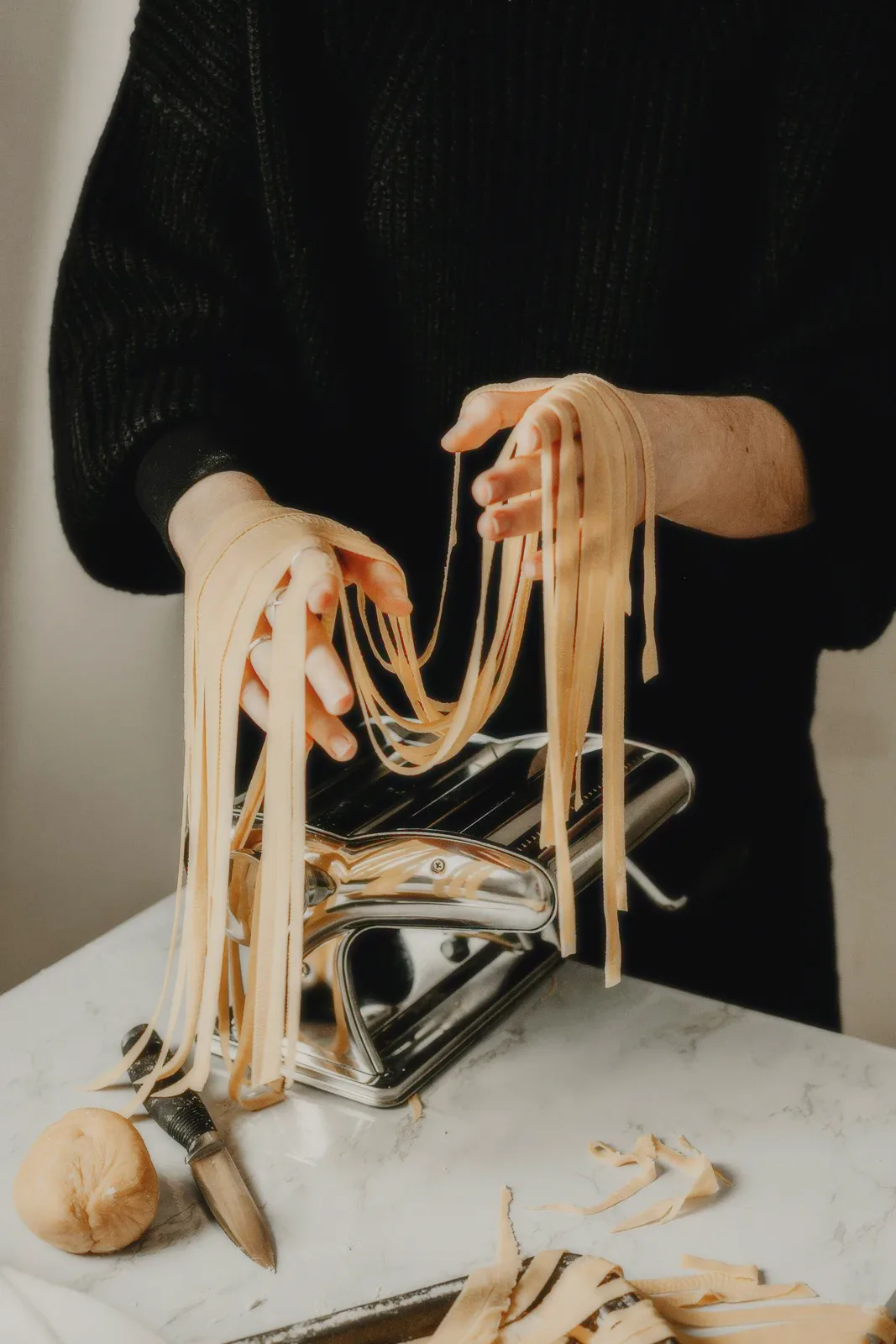 Hands lifting fresh tagliatelle from a pasta machine.