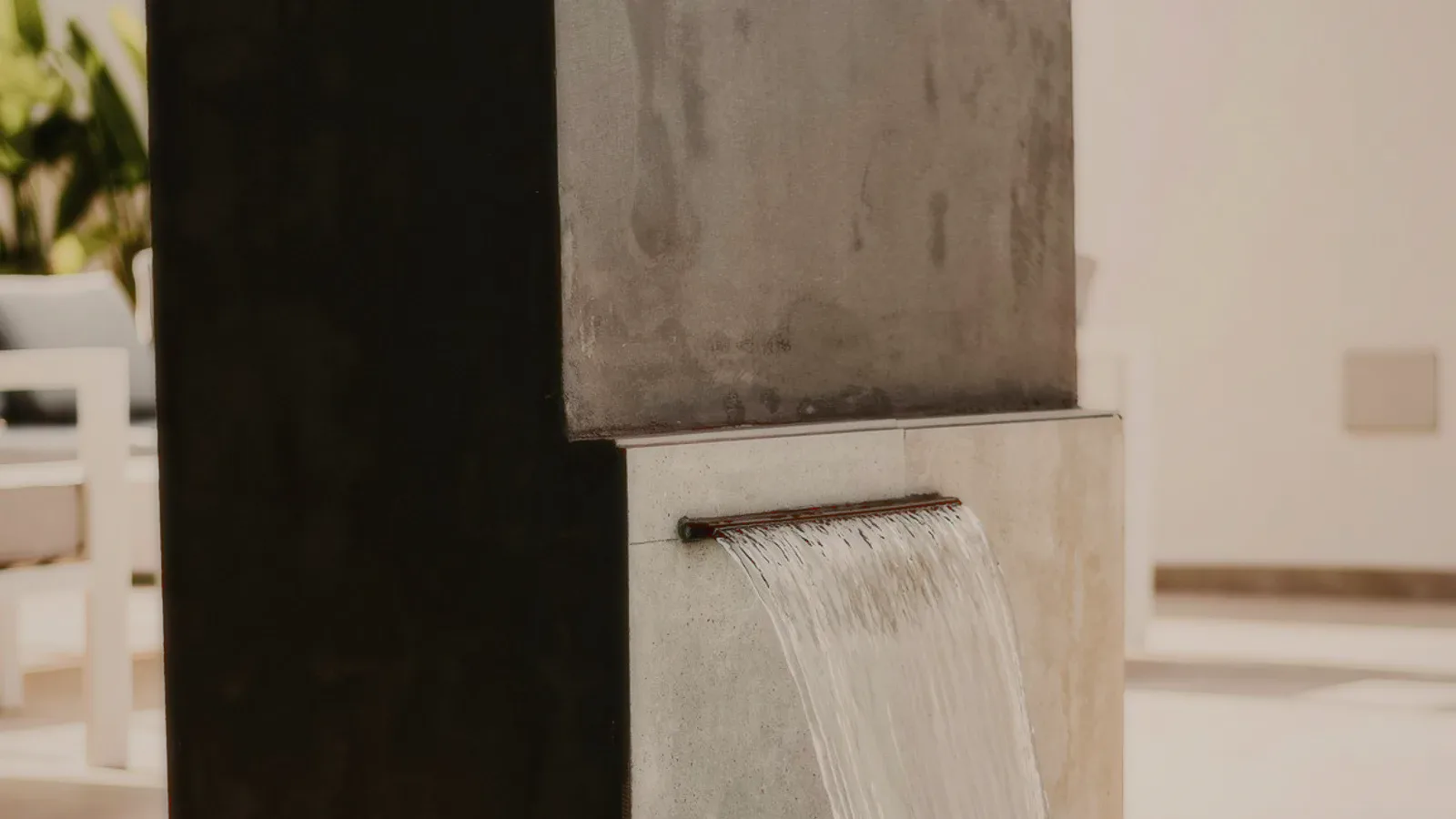 A sheet of water falling from a stone wall into a pool.