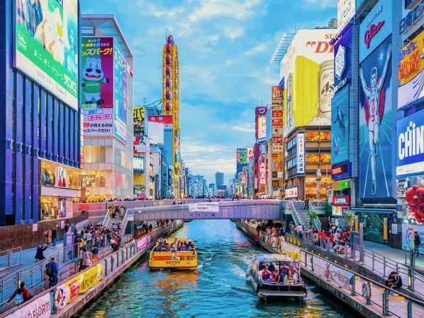Boats on the Dotonbori canal in Osaka, between walls of signs.