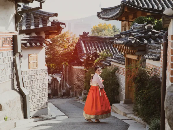 A woman in hanbok walking between old houses in Seoul.