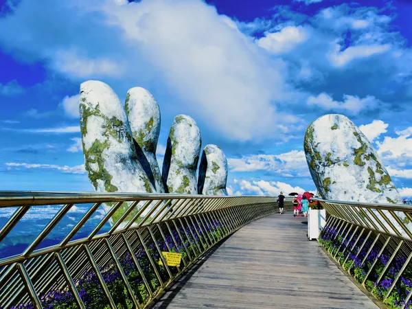 The Golden Bridge held by two stone hands, under a blue sky.