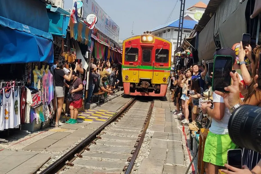 A train passing between market stalls while visitors take photographs.