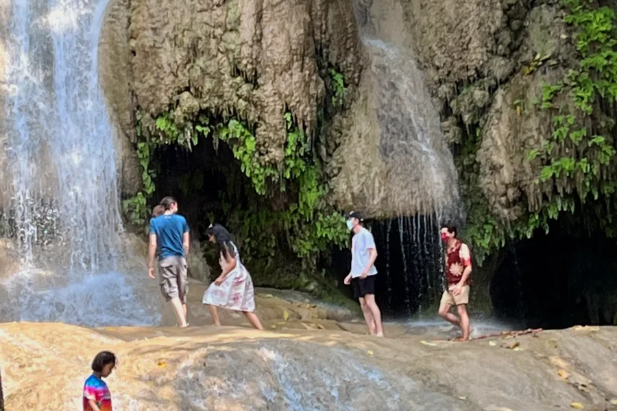 Visitors standing on the rocks under a waterfall.
