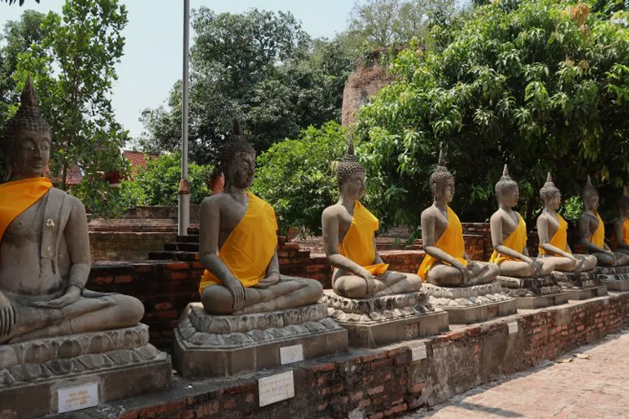 A row of seated stone Buddhas wearing saffron cloth.