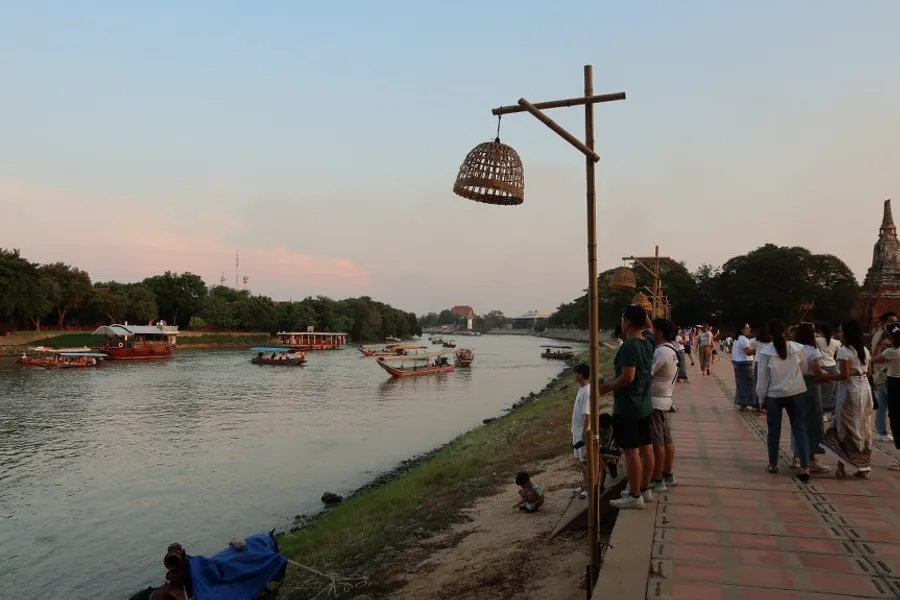 People walking beside the river in Ayutthaya at dusk.