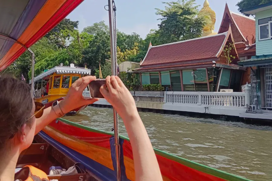 A traveller taking a photograph of a temple from a longtail boat.