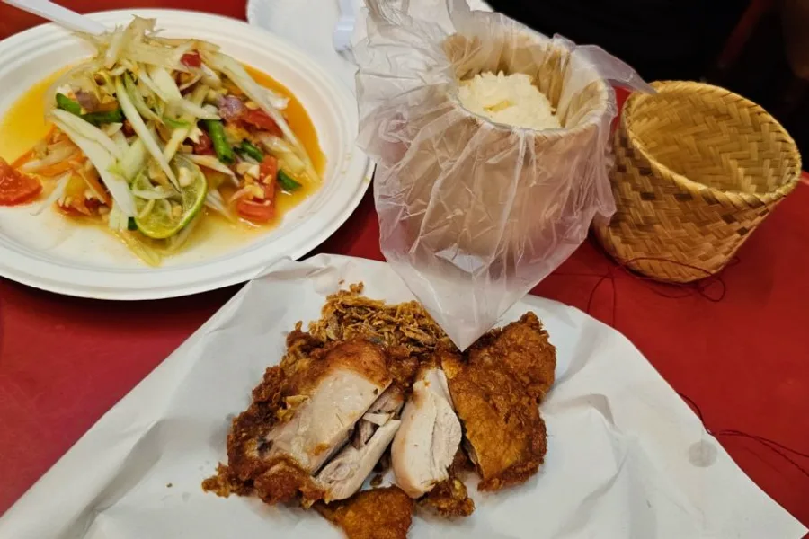 A plate of papaya salad and fried chicken with sticky rice.