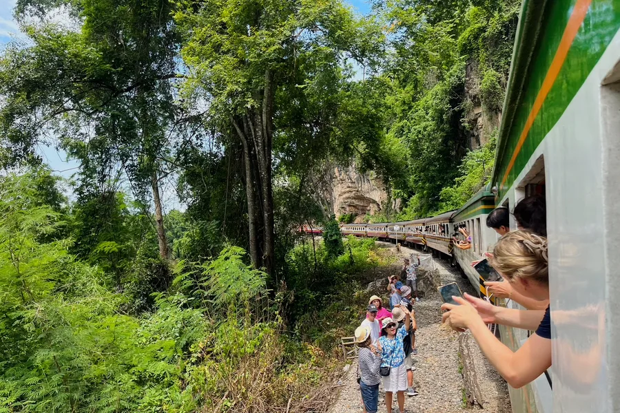 Travellers leaning from a train window beside a cliff.