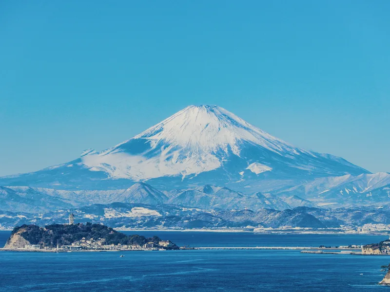 Mount Fuji with snow on its top, seen across the sea.