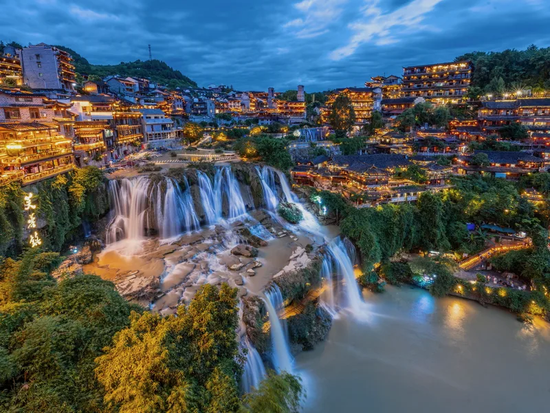 The old town of Furong above its waterfall at dusk.