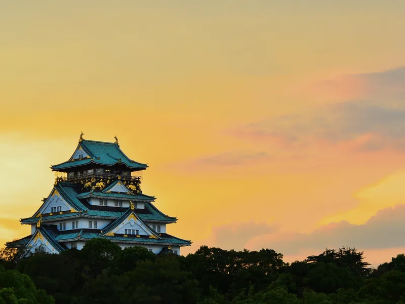 Osaka Castle above the trees at sunset.