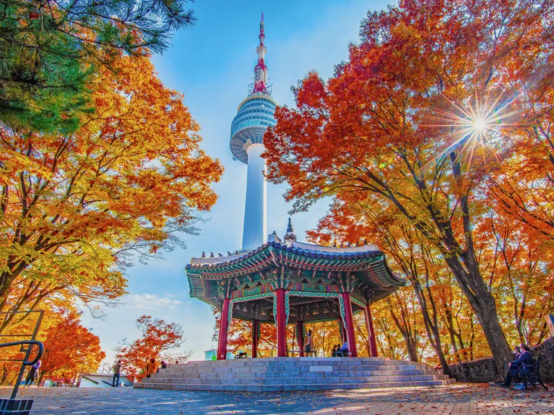 N Seoul Tower seen between red and orange autumn trees.